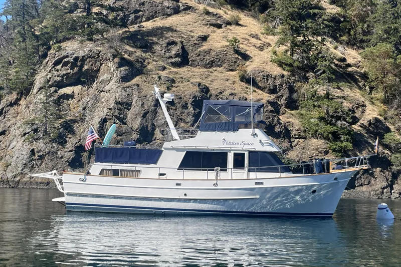 Slide: The Image of 1987 DeFever Trawler boat anchored near rocky shoreline with trees. - 50