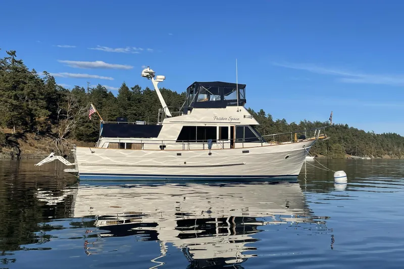 The Image of 1987 DeFever Trawler anchored on calm water with scenic forest backdrop. - 0