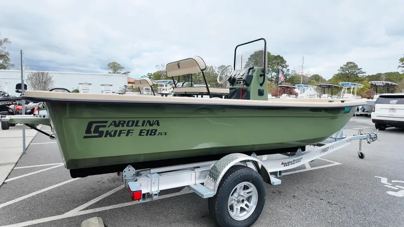 Slide: The Image of 2025 Carolina Skiff E18 JVX CC Swamp Edition boat on trailer in parking lot. - 2