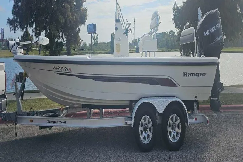 The Image of 2009 Ranger 2200 Bay Ranger boat on trailer by a lake, featuring Mercury outboard motor. - 0
