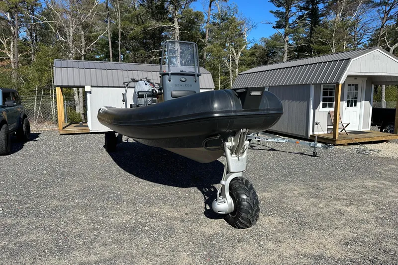 Slide: The Image of 2019 Sealegs 7.1 RIB amphibious boat parked on gravel near sheds. - 2