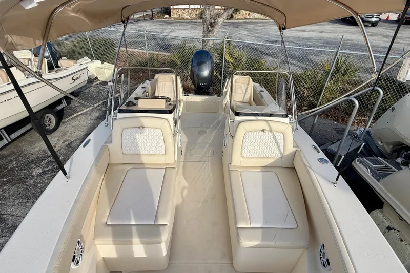 Slide: The Image of 2026 Scout 195 Sport Dorado boat with beige seating and canopy, parked outdoors. - 10