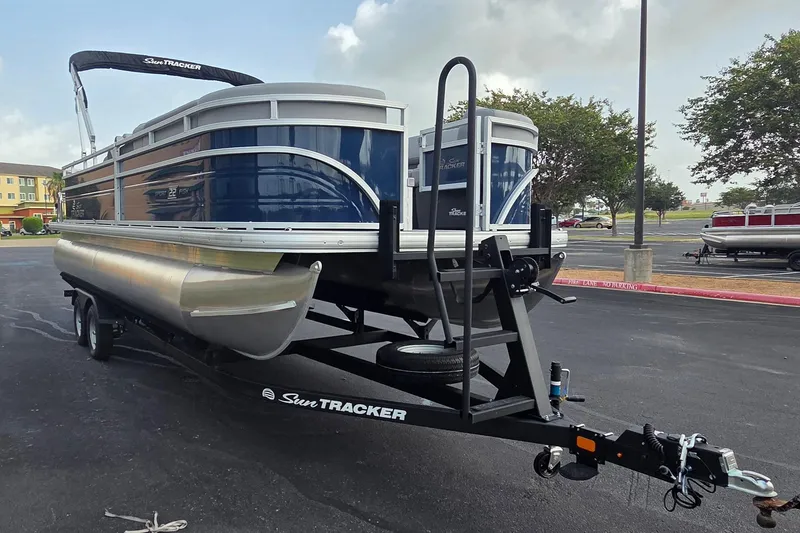Slide: The Image of 2026 Sun Tracker SportFish 22 DLX pontoon boat on trailer in parking lot. - 2