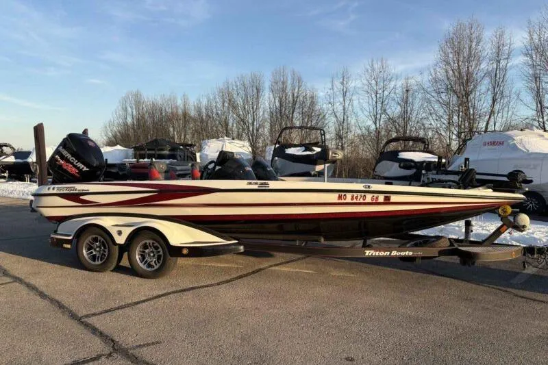 Slide: The Image of 2015 Triton 22 TrX boat on trailer, parked outdoors with trees in background. - 0