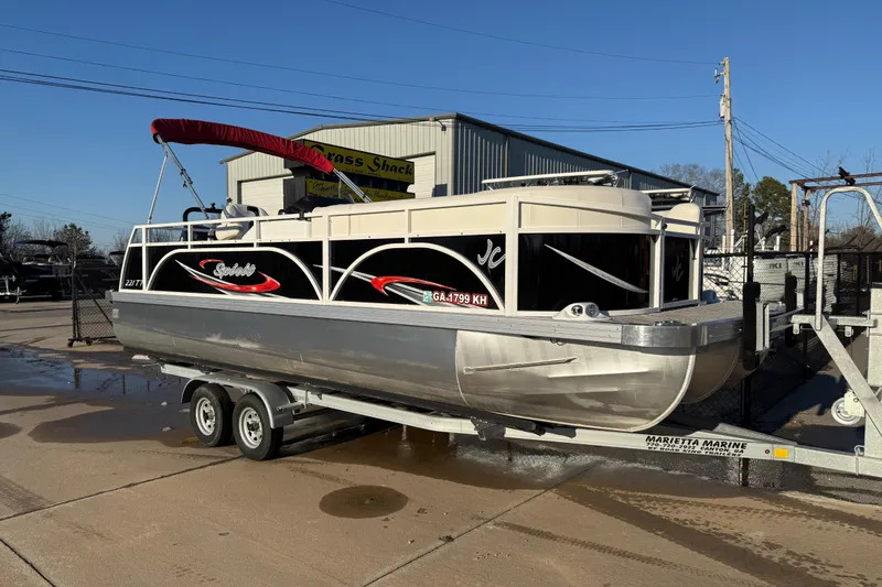 The Image of 2021 JC Spirit 221TT pontoon boat on trailer at marina under clear blue sky. - 0