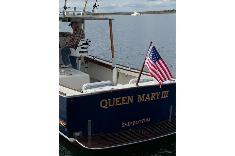 Slide: The Image of 1982 SISU 26 boat "Queen Mary III" with American flag on calm water. - 2