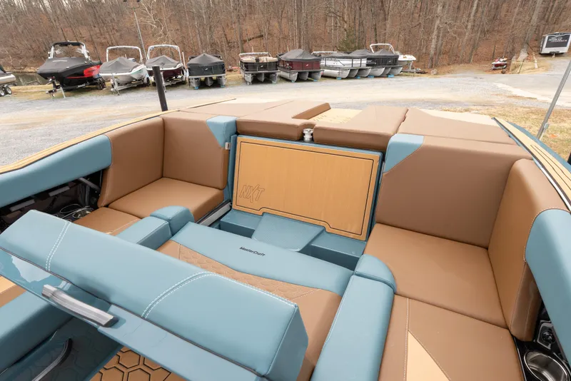 Slide: The Image of 2026 MasterCraft NXT23 boat interior with tan and blue seating, docked near other boats. - 6