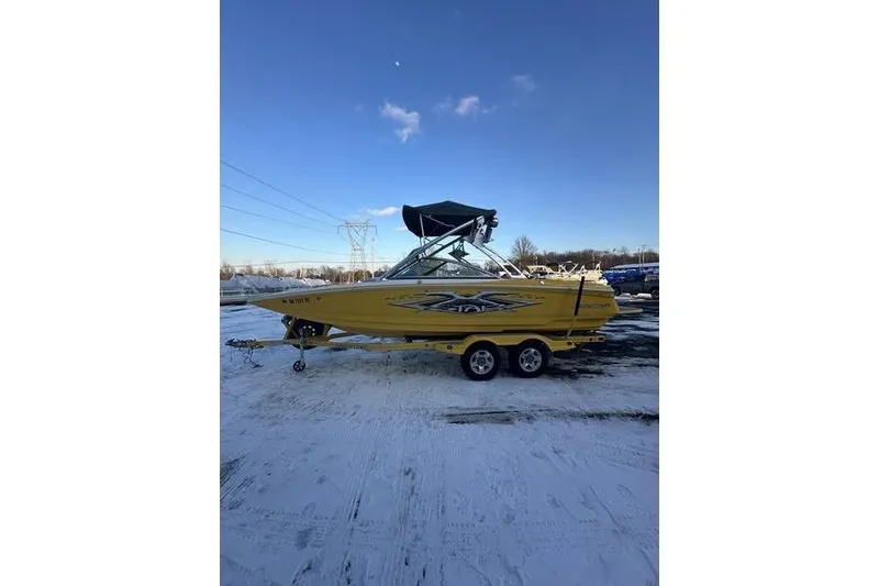 Slide: The Image of 2004 MasterCraft XStar 23 yellow boat on trailer, parked on snowy ground under clear blue sky. - 15