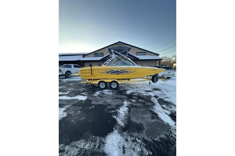 Slide: The Image of Yellow 2004 MasterCraft XStar 23 boat on trailer, parked outside dealership in snowy setting. - 6