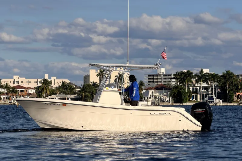 The Image of 2020 Cobia 220 Center Console boat on water, cityscape background, American flag flying. - 0