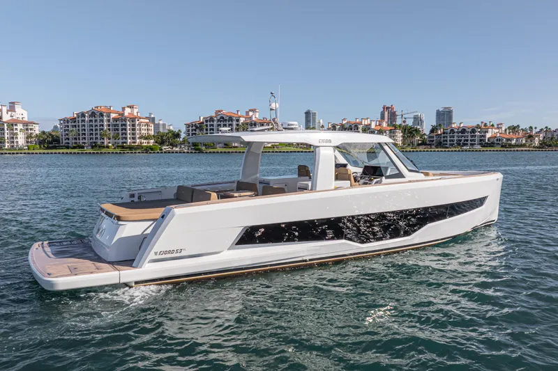 Slide: The Image of 2024 Fjord Boats 53XL cruising on water with luxury waterfront buildings in the background. - 8