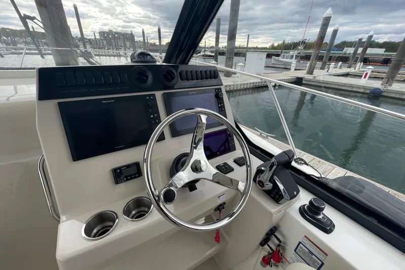 Slide: The Image of 2023 Boston Whaler 325 Conquest helm with dual screens and steering wheel at marina. - 10
