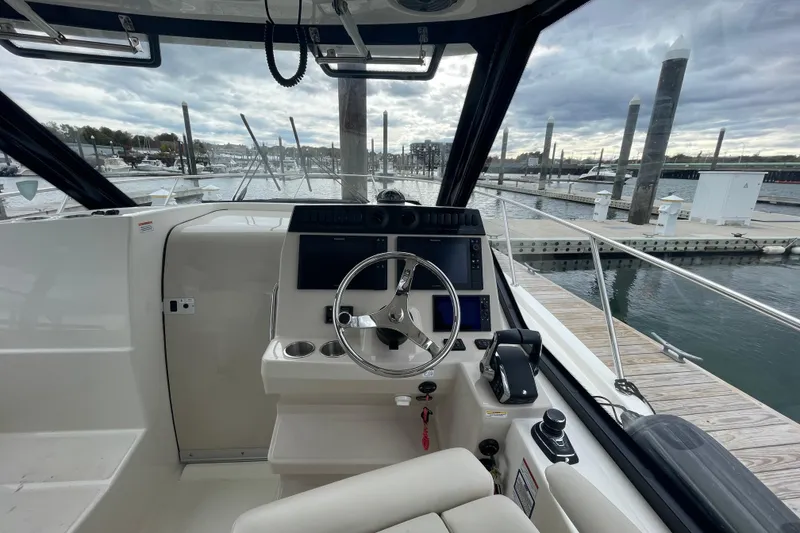 Slide: The Image of 2023 Boston Whaler 325 Conquest helm with marina view, featuring modern controls and steering. - 9