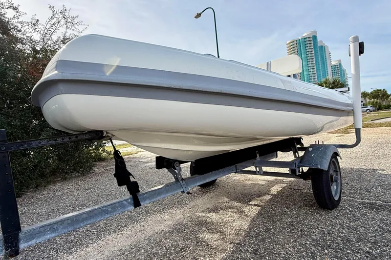 Slide: The Image of 2023 Rigid Boats 10 Sport on trailer, parked near modern buildings. - 5