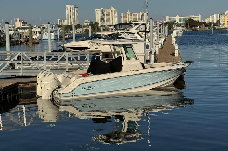 Slide: The Image of 2023 Boston Whaler 250 Outrage docked at marina with city skyline background. - 2