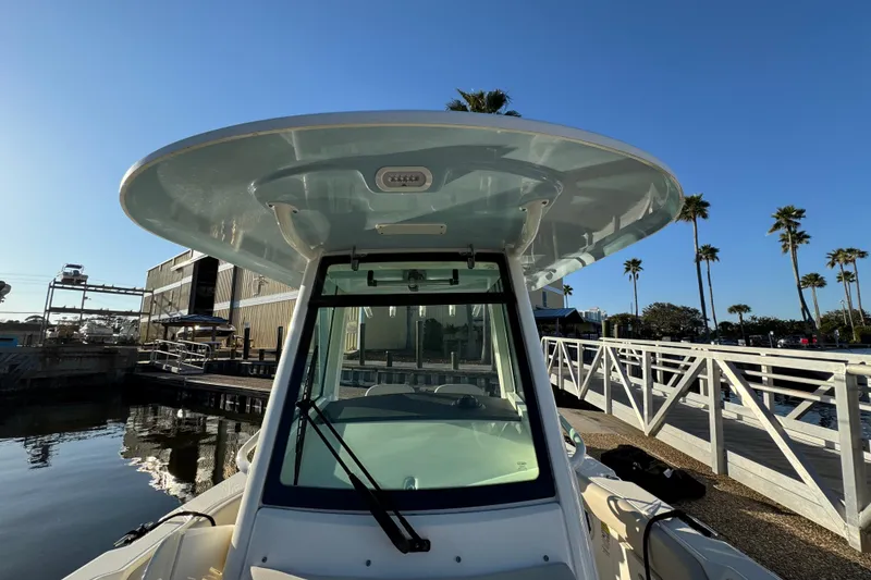 Slide: The Image of 2023 Boston Whaler 250 Outrage boat docked, showcasing helm and T-top under clear blue sky. - 24