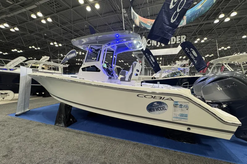 Slide: The Image of 2026 Cobia 245 Center Console boat displayed at an indoor boat show. - 2