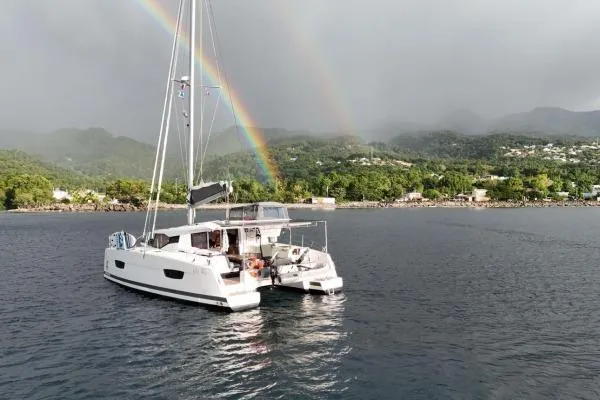 The Image of 2023 Fountaine Pajot Isla 40 catamaran sailing under a double rainbow near lush coastline. - 0