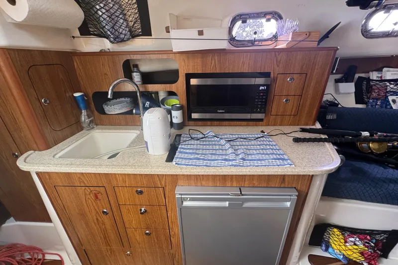 Slide: The Image of 2014 Pursuit OS 345 Offshore boat interior with kitchenette, sink, microwave, and storage cabinets. - 59