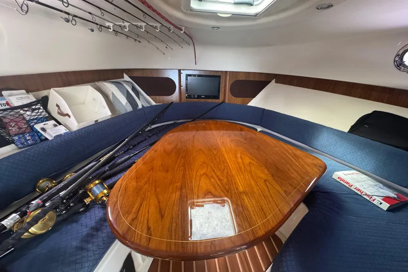 Slide: The Image of 2014 Pursuit OS 345 Offshore cabin with fishing rods, wooden table, and blue seating. - 68
