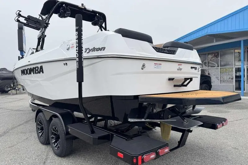 Slide: The Image of 2026 Moomba Tykon boat on trailer, white exterior, parked near blue building. - 6