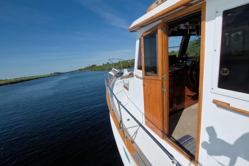 Slide: The Image of 1980 Kadey-Krogen 42 trawler cruising on a serene waterway under clear blue skies. - 20