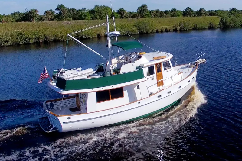Slide: The Image of 1980 Kadey-Krogen 42 trawler cruising on a calm river, surrounded by lush greenery. - 3