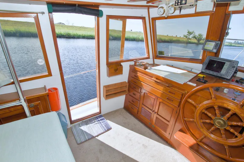Slide: The Image of 1980 Kadey-Krogen 42 trawler helm with wooden wheel, navigation equipment, and scenic water view. - 34