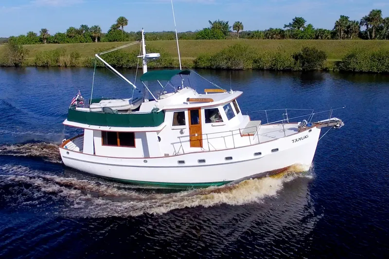 Slide: The Image of 1980 Kadey-Krogen 42 trawler cruising on a serene river with lush greenery. - 4