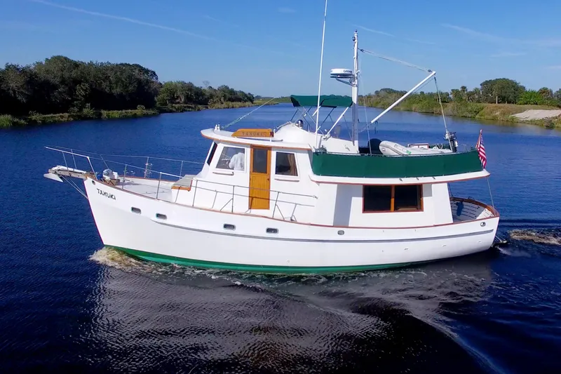 Slide: The Image of 1980 Kadey-Krogen 42 trawler cruising on a serene river under a clear blue sky. - 8
