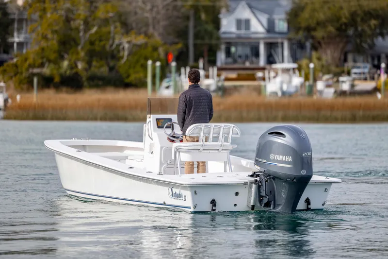 Slide: The Image of 2025 Intruder 23 boat with Yamaha engine on calm water, near shoreline homes. - 5