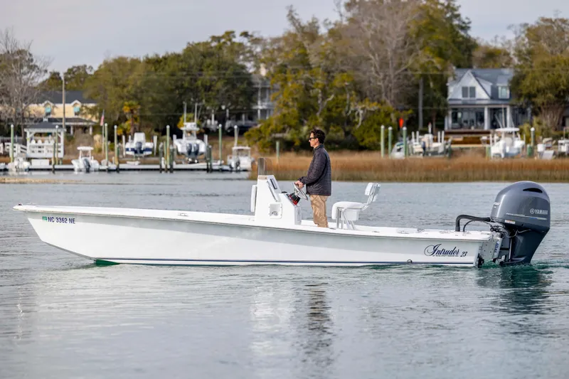 Slide: The Image of 2025 Intruder 23 boat on calm water with a person steering near a marina. - 7