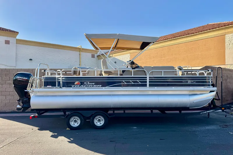 The Image of 2022 Sun Tracker Fishin' Barge 22 DLX pontoon boat on trailer, parked outdoors. - 0