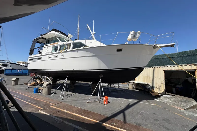 Slide: The Image of 1977 Bertram 42 Flybridge Motor Yacht on stands in a boatyard under clear blue sky. - 2