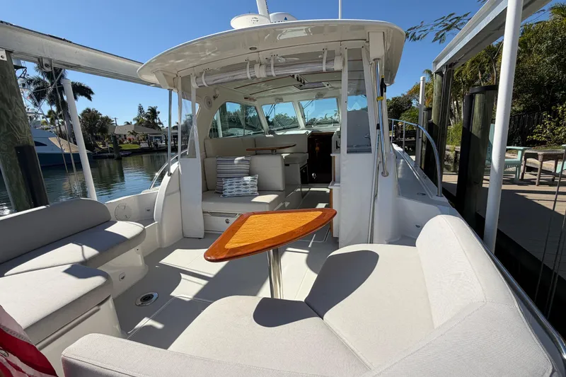 Slide: The Image of 2023 Back Cove 340 boat interior with seating and wooden table, docked by a scenic waterfront. - 25