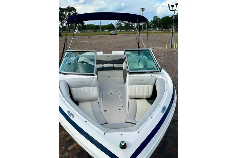 Slide: The Image of 2012 Regal 2100 Bowrider boat with white seating and blue canopy in a parking area. - 3