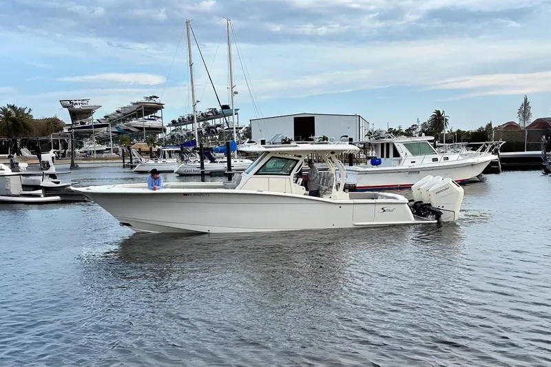 The Image of 2023 Scout 355 LXF boat on water, docked at marina with other vessels. - 1