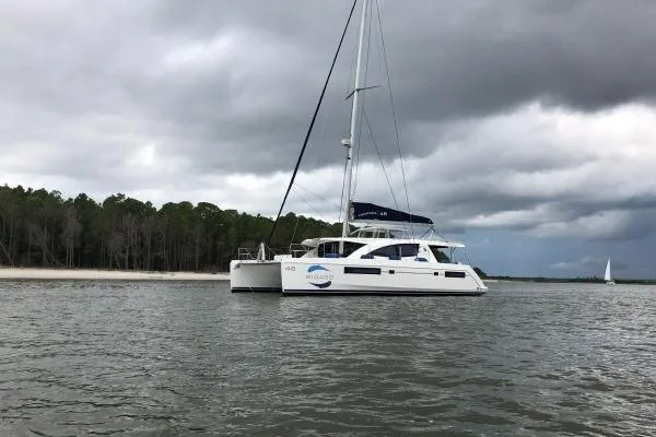 Slide: The Image of 2015 Leopard 48 catamaran sailing near a forested shoreline under cloudy skies. - 74
