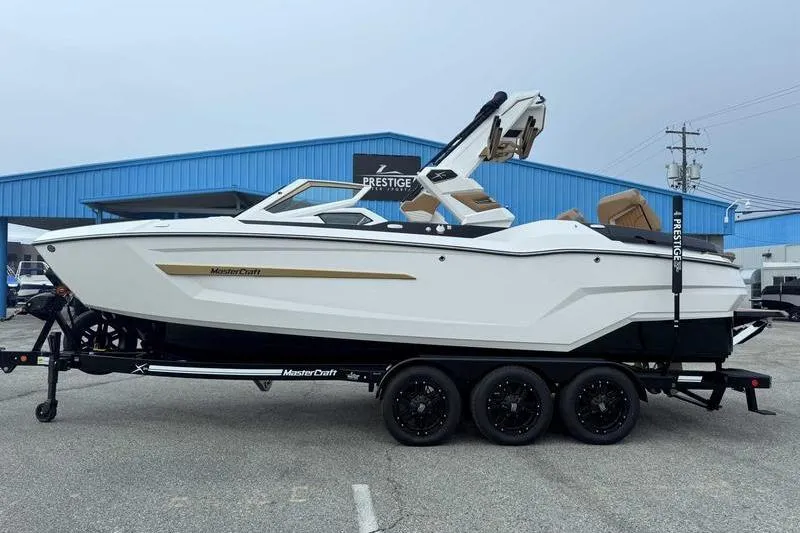 The Image of 2026 MasterCraft X24 boat on trailer, parked outside a blue building. - 1