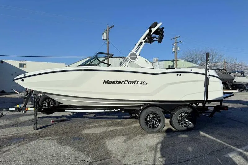 The Image of 2026 MasterCraft NXT20 boat on trailer, parked outdoors under clear blue sky. - 1