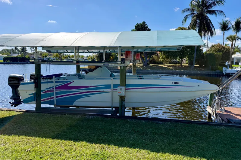 Slide: The Image of 2001 Cobra Predator 3100 boat on lift by waterfront, under canopy, with palm trees in background. - 27