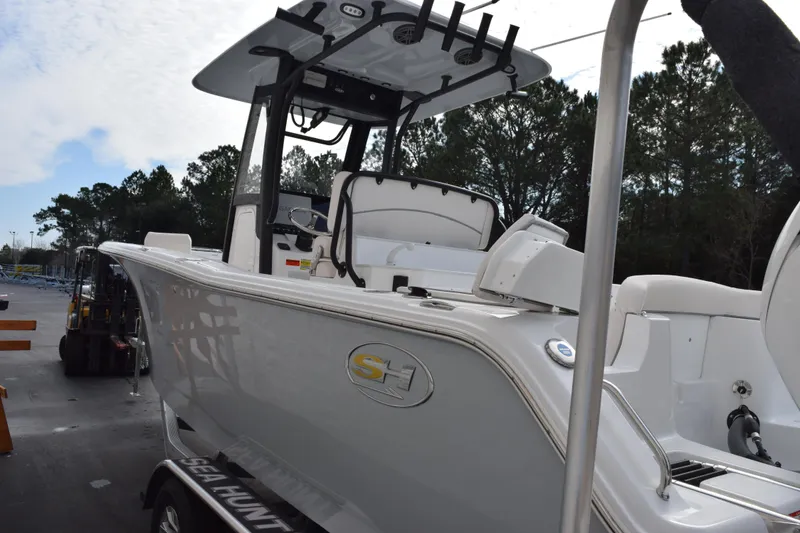 Slide: The Image of 2026 Sea Hunt Ultra 245 SE boat, sleek design, parked outdoors with trees in the background. - 6