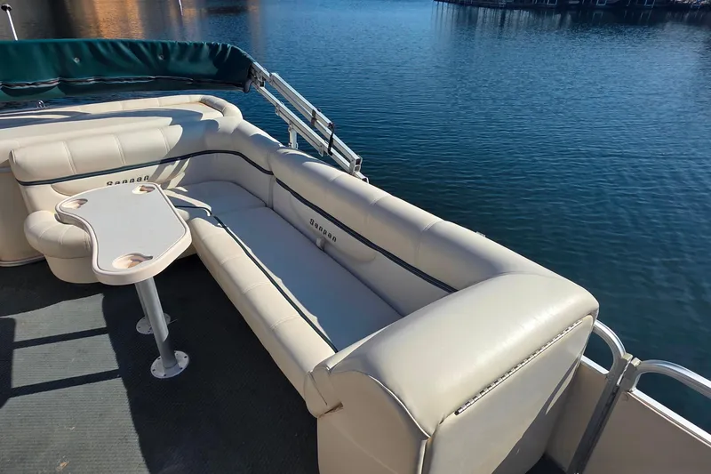 Slide: The Image of 2004 Sanpan 2500 RE pontoon boat interior with beige seating and table on a calm lake. - 12