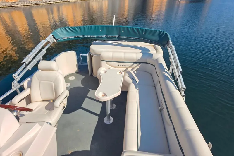 Slide: The Image of 2004 Sanpan 2500 RE pontoon boat interior with seating and table on calm water. - 14