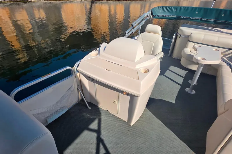 Slide: The Image of 2004 Sanpan 2500 RE pontoon boat interior with beige seating on a calm lake. - 19