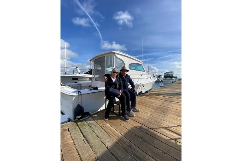 Slide: The Image of Couple sitting on dock beside 1999 Mainship Pilot 30 boat under blue sky. - 15