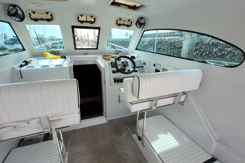 Slide: The Image of 1999 Mainship Pilot 30 interior view at dock, featuring white seating and clear windows. - 6