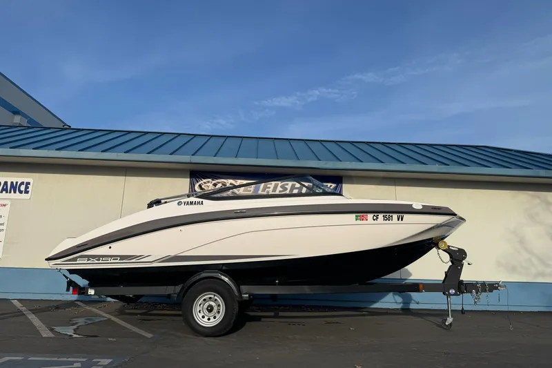 The Image of 2022 Yamaha Boats SX190 on trailer, parked outdoors under clear blue sky. - 1