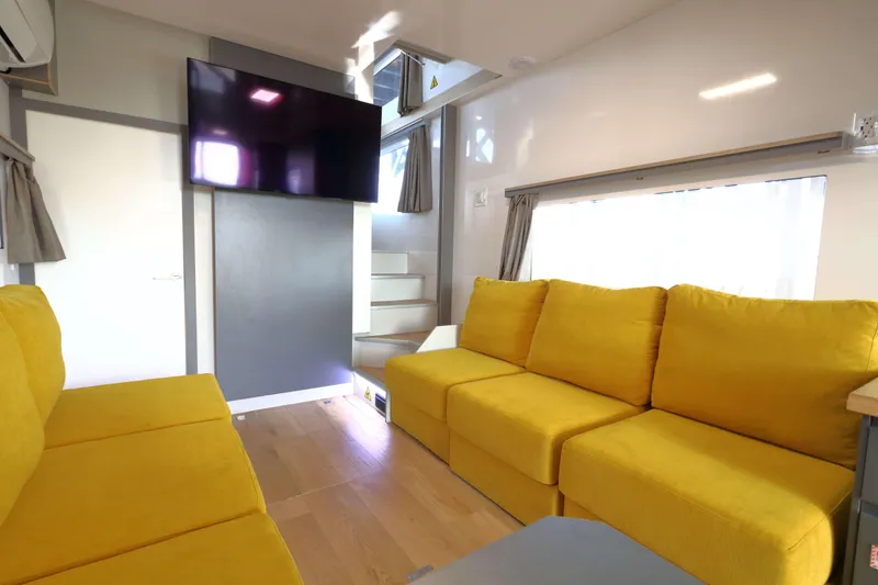 Slide: The Image of Modern Navisyo Homes NV.08 interior with yellow sofas, TV, and stairs, 2021 model. - 3