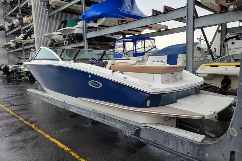 Slide: The Image of 2016 Cobalt CS3 boat in storage, blue and white design, docked on a rainy day. - 2
